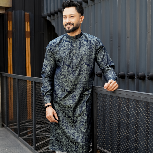 A man wearing a green and blue jacquard cotton panjabi with floral patterns, standing near a black fence.