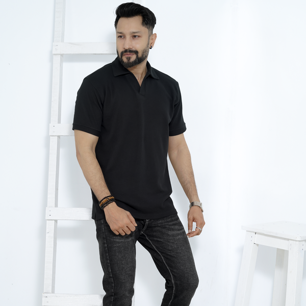 Man wearing a black polo shirt and dark jeans against a white background