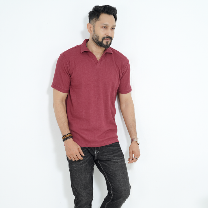 Man wearing a maroon color polo shirt and dark jeans against a white background