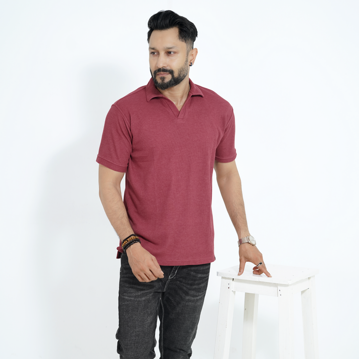 Man wearing a maroon polo shirt and dark jeans against a white background