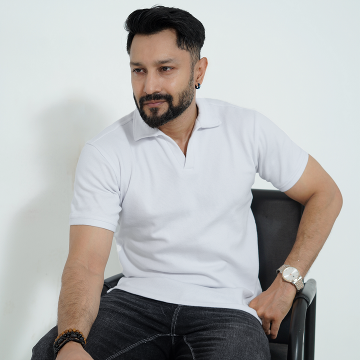 Man wearing a white polo shirt and black pants sitting on a chair against a white background