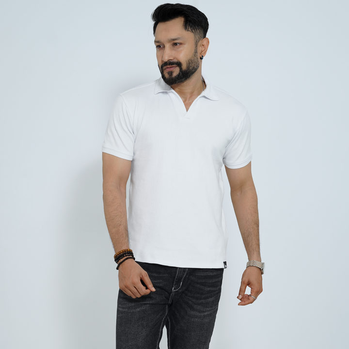 Man wearing a white polo shirt and dark jeans against a light gray background