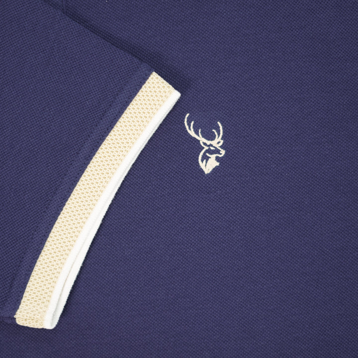 Navy blue polo shirt with beige trim and a white embroidered logo on a dark background