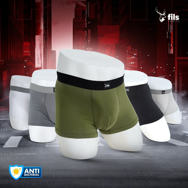 Three pairs of men's underwear in green, black, and gray on a futuristic cityscape background with 'fils' branding.